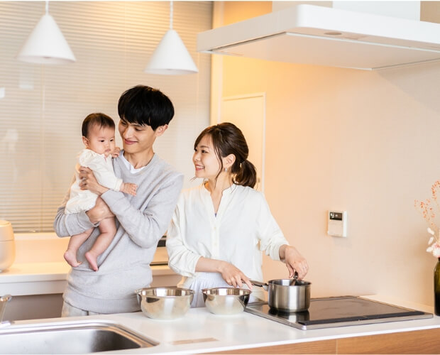 オープンキッチンで子どもを抱きながら料理をする夫婦